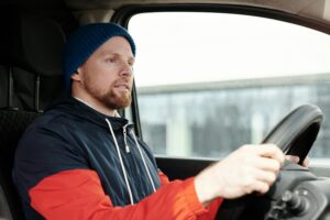 A bearded man wearing a hoodie and knitted cap driving a car, focused and attentive.