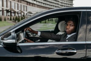 African American man confidently driving a sleek black luxury car outside a modern building.